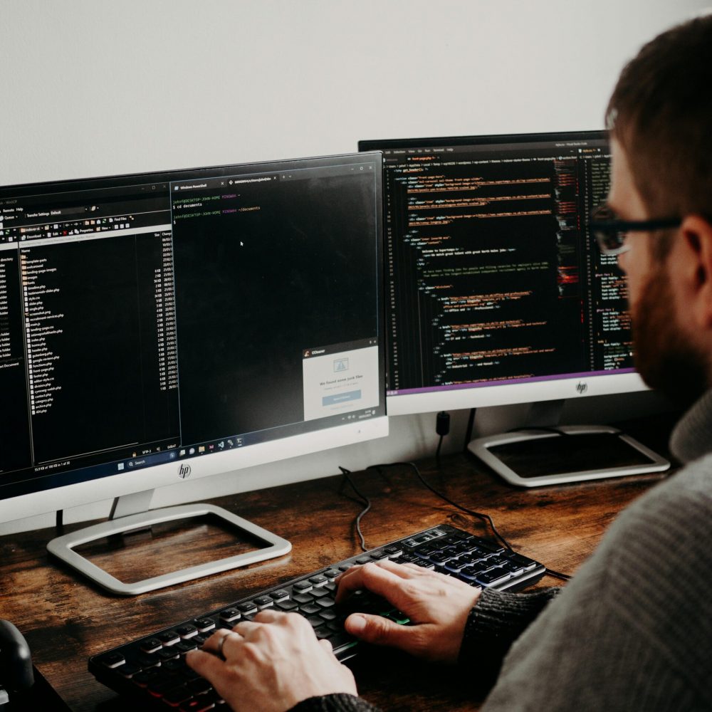 Software developer working on dual monitors with code displayed — representing A Team Professional Associates’ Software Solutions services.
